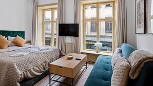 A hotel room with a bed, a sofa, a TV, a table, and a window with curtains. - Charming Apartment in Old Town (Stockholm)