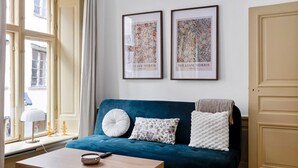A room with a blue sofa, two framed artworks, a wooden coffee table, and a window with curtains. - Charming Apartment in Old Town (Stockholm)