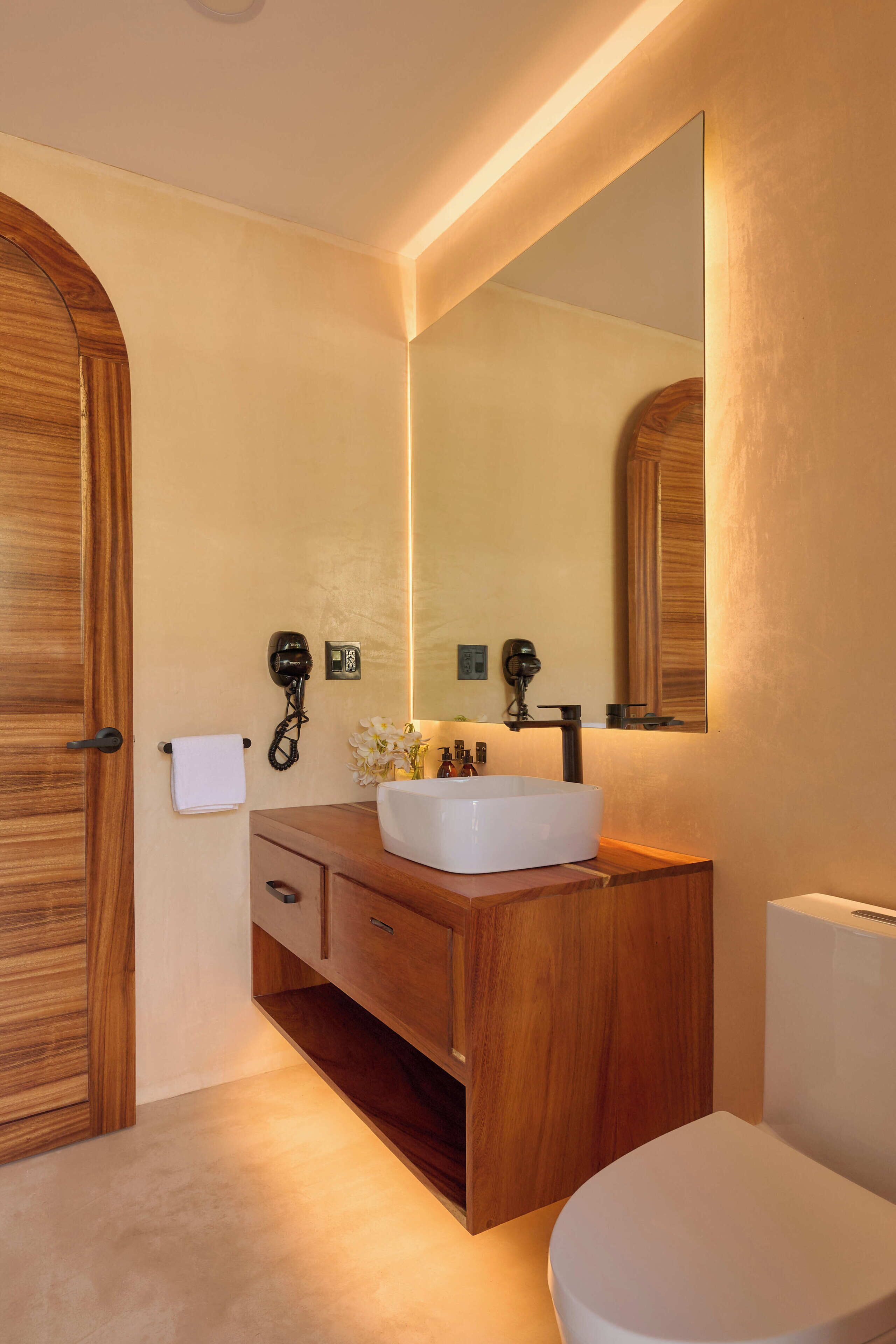 A bathroom with a wooden vanity, a white sink, a large mirror, and a toilet.