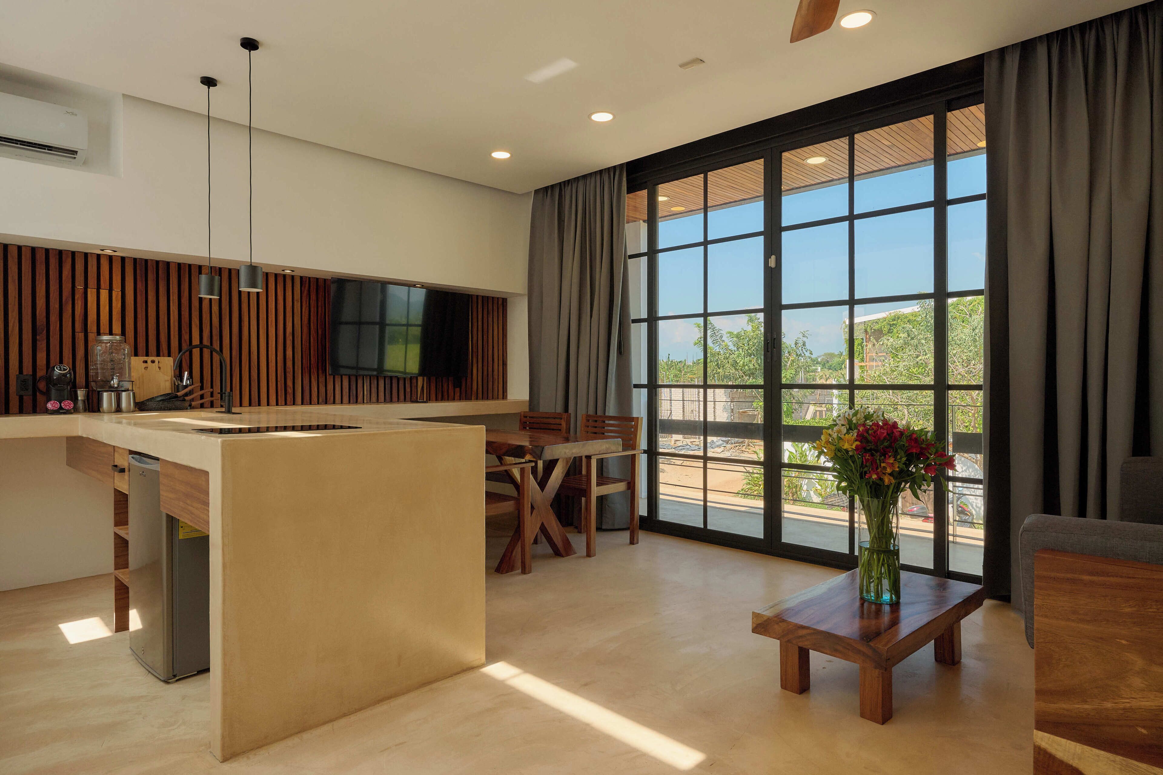 A modern kitchen with a central island, dining area with wooden furniture, and large windows with curtains.