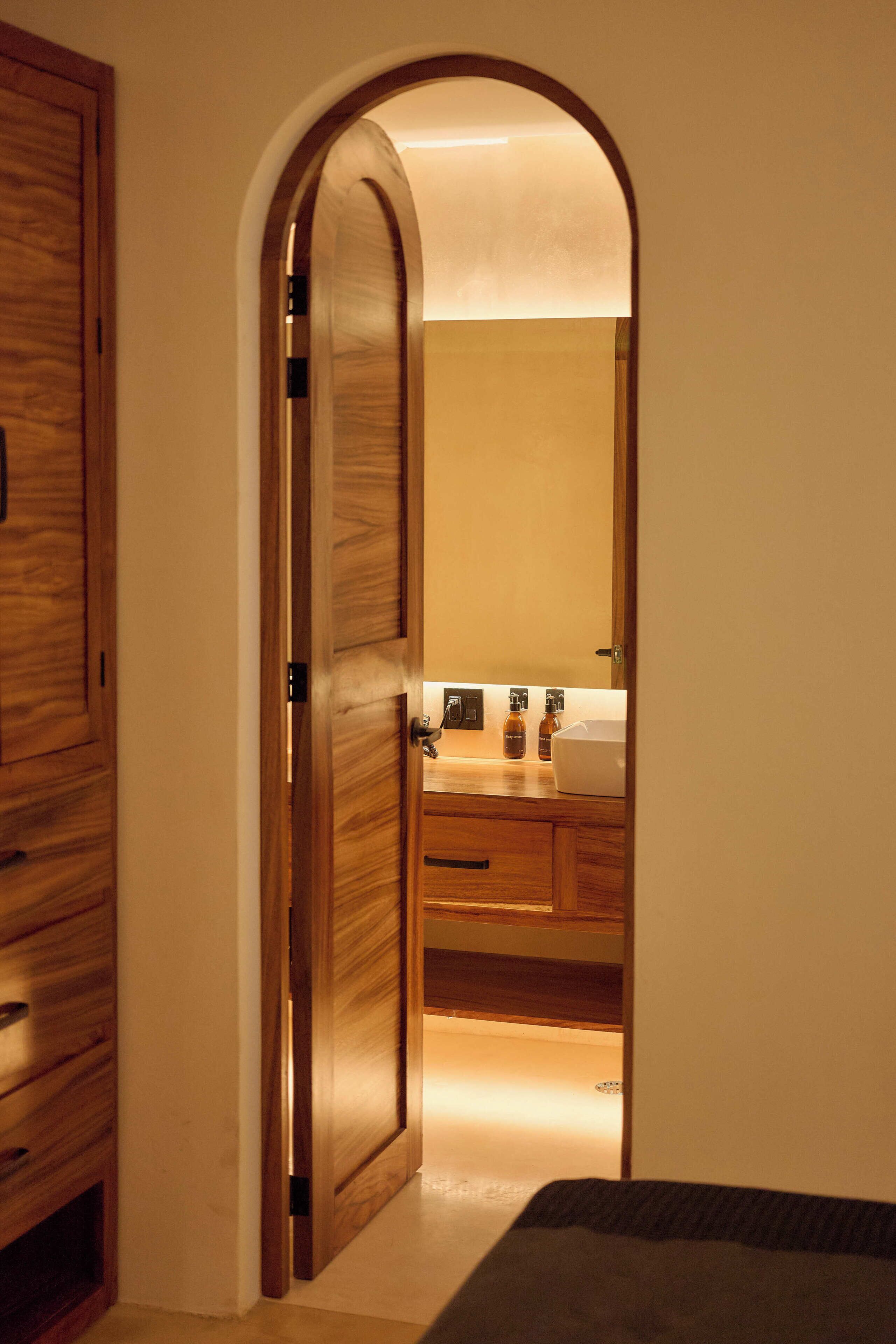 A wooden door leading to a bathroom with a sink and mirror.
