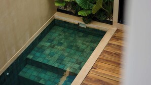 A rectangular pool with a wooden deck surrounding it, a small step leading into the pool, and large green plants against the wall. - Hotel Compatir (Santa María Colotepec)