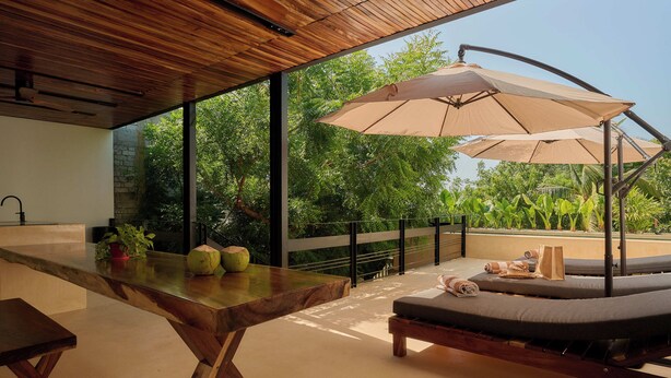 A modern outdoor seating area with a wooden table, lounge chairs, and a large umbrella. - Hotel Compatir (Santa María Colotepec)