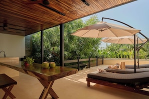 A modern outdoor seating area with a wooden table, lounge chairs, and a large umbrella.