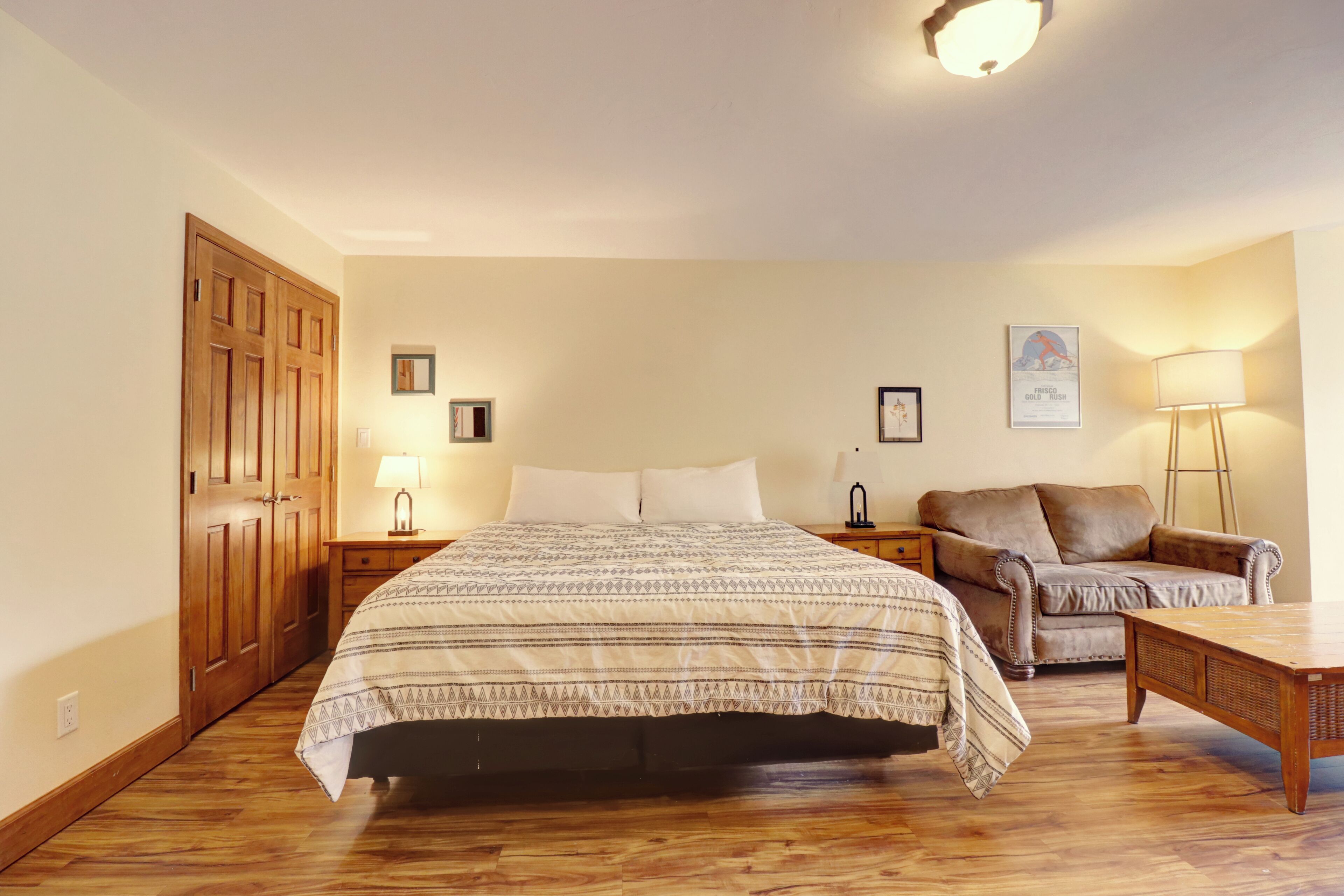 A bedroom with a bed, a wooden wardrobe, a sofa, a coffee table, and a lamp.