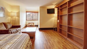 Un dormitorio con una cama, un armario de madera, un televisor y una ventana con vistas a montañas.
