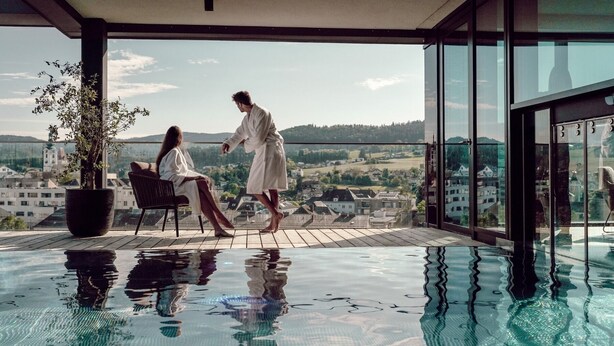 A couple in a modern indoor pool with a city view. - Hotel FREIGOLD (Freistadt)