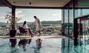 A couple in a modern indoor pool with a city view. - Hotel FREIGOLD (Freistadt)