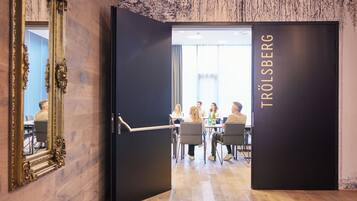 A conference room with a wooden floor, a large mirror, and a door leading to a meeting area with tables and chairs.