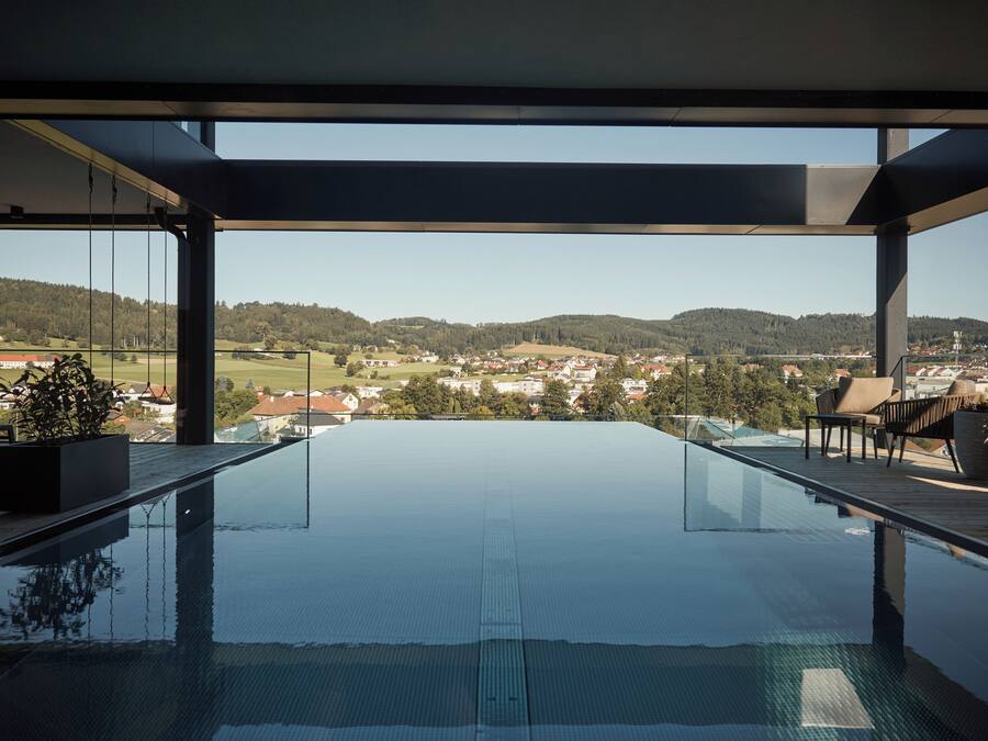 A modern infinity pool with a clear view of a town and hills in the background.