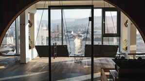 A modern interior with a large arched window, a swing chair, a small table, and a sofa. - Hotel FREIGOLD (Freistadt)