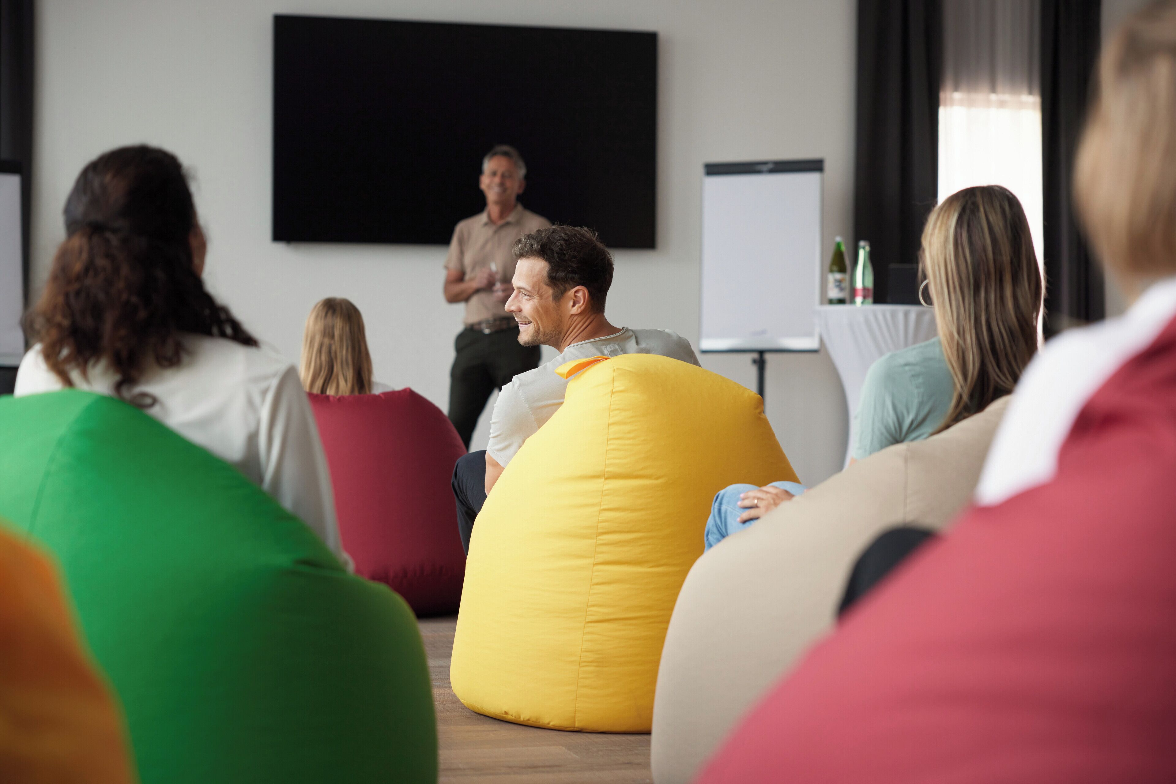 A group of people seated on colorful bean bags in a room with a large screen at the front.