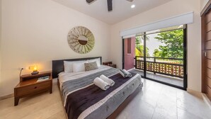 A bedroom with a bed, a nightstand, a ceiling fan, a large window with a view of greenery, and a decorative wall piece. - Spacious 2BR Condo with Pool & Private Balcony (Tulum)