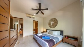 A bedroom with a large bed, a ceiling fan, a wall clock, and a bedside table with a lamp. - Spacious 2BR Condo with Pool & Private Balcony (Tulum)