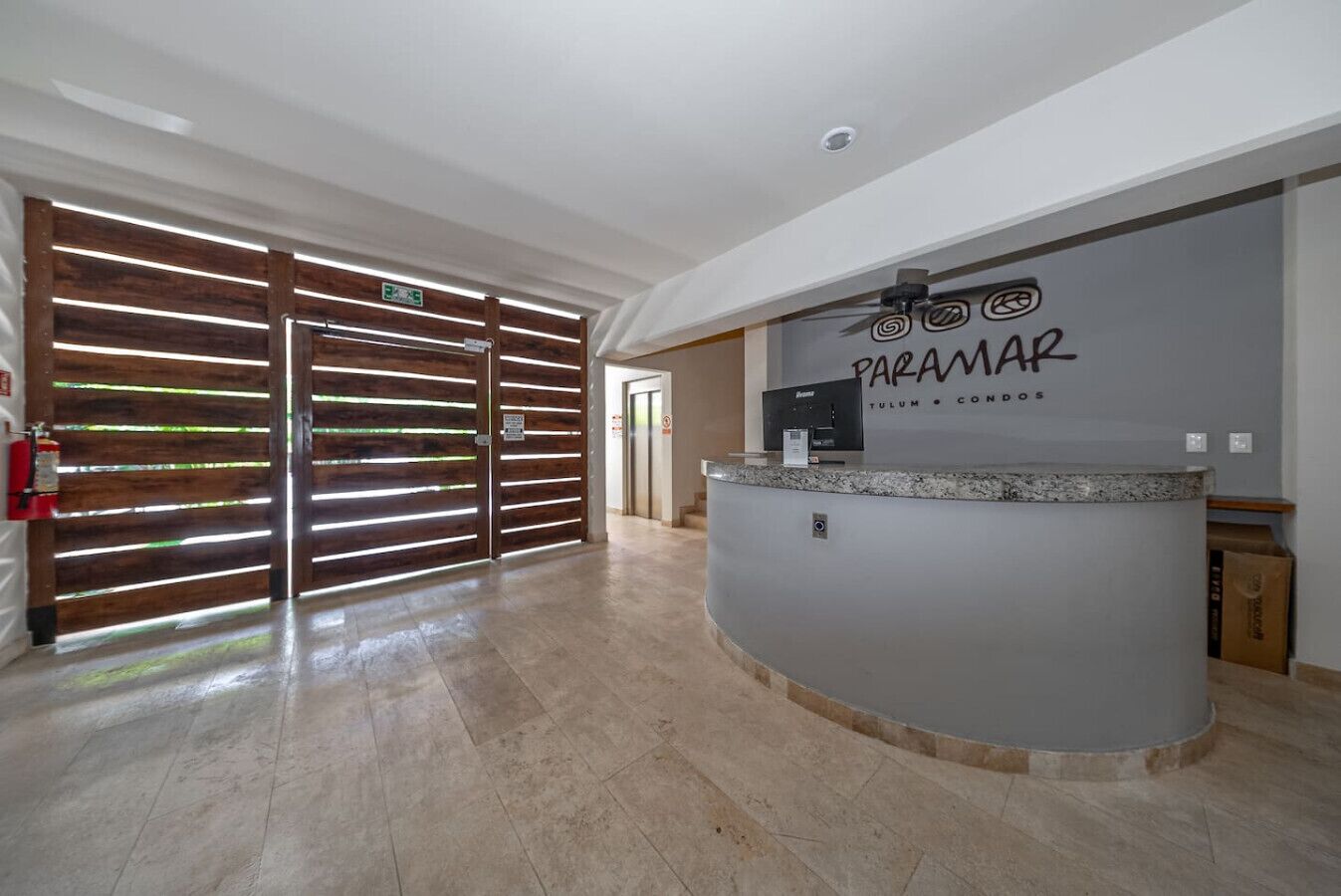 Un espace d’accueil doté d’une porte coulissante en bois, d’un comptoir de réception et d’une enseigne indiquant : « PARAMAR TULUM – APPARTEMENTS ».