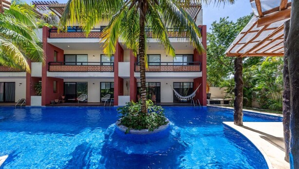 A hotel with a swimming pool, palm trees, and a two-story building with balconies. - Spacious 2BR Condo with Pool & Private Balcony (Tulum)
