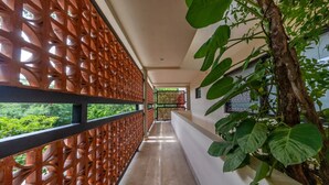 A corridor with a wooden lattice partition, a view of greenery outside, and a plant on the right. - Spacious 2BR Condo with Pool & Private Balcony (Tulum)