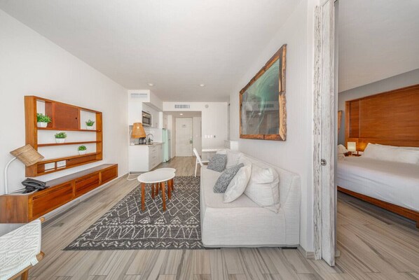 A modern hotel room with a white sofa, a small dining table, a wooden console table, and a large mirror. - Modern 1BR w/Rooftop Pool-Walk to Beach & 5th Ave (Playa del Carmen)