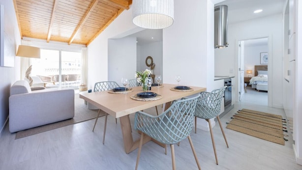 A modern dining area with a wooden table, light blue chairs, and a hanging light fixture. - Casa Gio Apartment - Praia da Luz (Luz)
