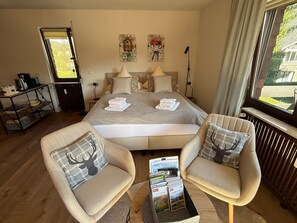A bedroom with a bed, two chairs, a coffee table, a radiator, a window, and artwork on the wall. - Apartment 'Niki' with Balcony and Wi-Fi (Titisee-Neustadt)