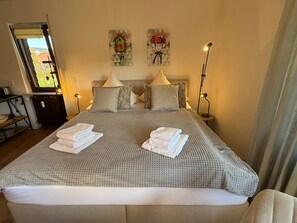 Un lit bien fait, agrémenté de serviettes, une tête de lit ornée de coussins décoratifs, une lampe de chevet et des œuvres d’art accrochées au mur.