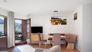 Una sala de estar moderna con suelo de madera, un sofá, una mesa de comedor y un televisor.