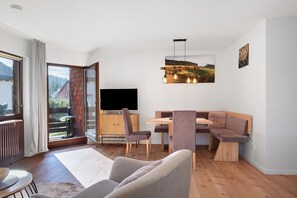 A modern living room with a wooden floor, a sofa, a dining table, and a TV.