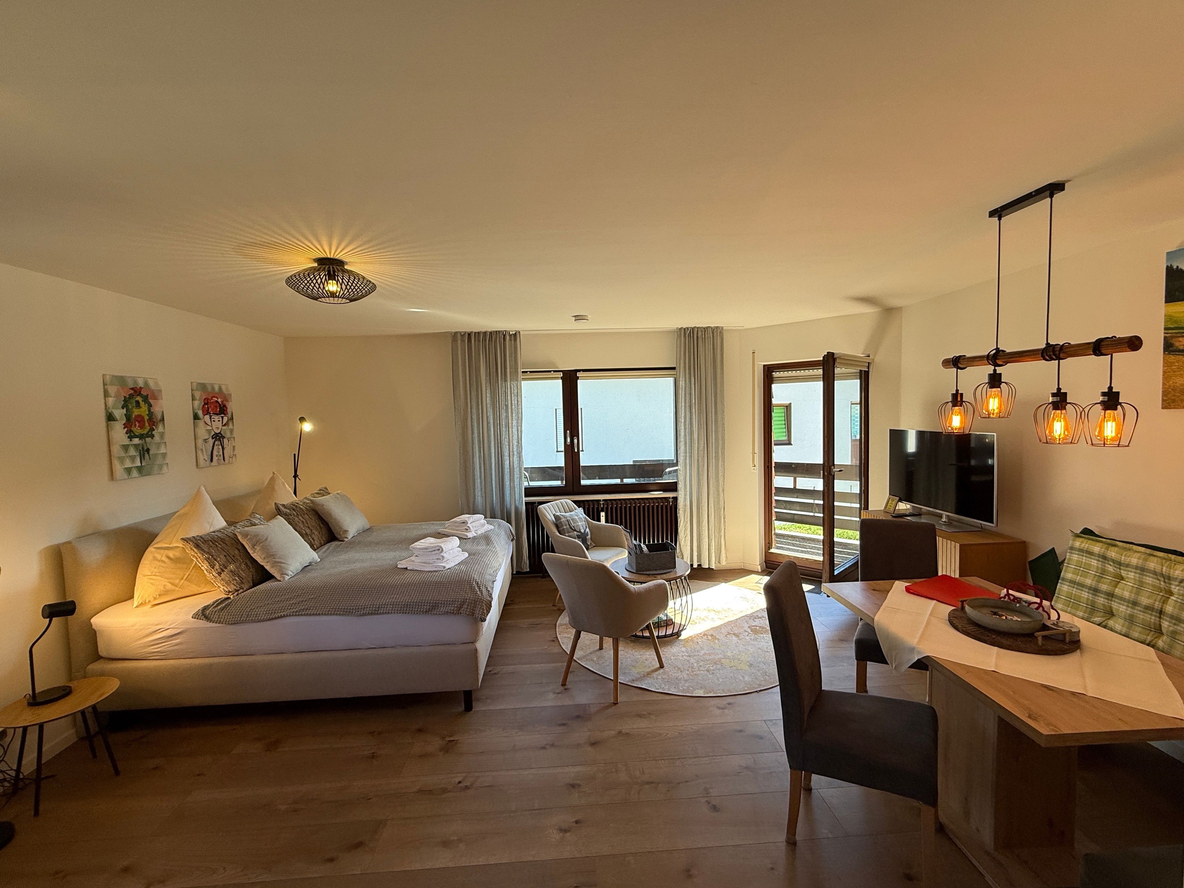 Een moderne hotelkamer met een bed, een bureau, een stoel, een televisie en een balkon met uitzicht.
