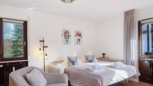 Un dormitorio con una cama, dos mesitas de noche, una silla, un radiador y una obra de arte en la pared.