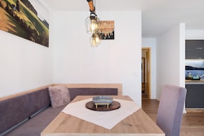 Uma área de refeições com mesa de madeira, uma tigela sobre apoio, um banco e uma luminária fixa na parede.