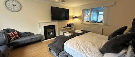 Een slaapkamer met een bed, een bank, een open haard, een televisie en een plafondventilator.