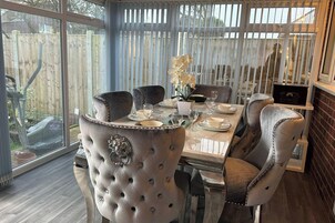 A dining area with a glass table set for six, surrounded by tufted chairs with decorative elements.