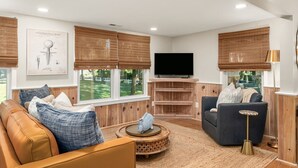 Uma sala de estar moderna com uma TV grande, dois sofás e um rack de madeira.