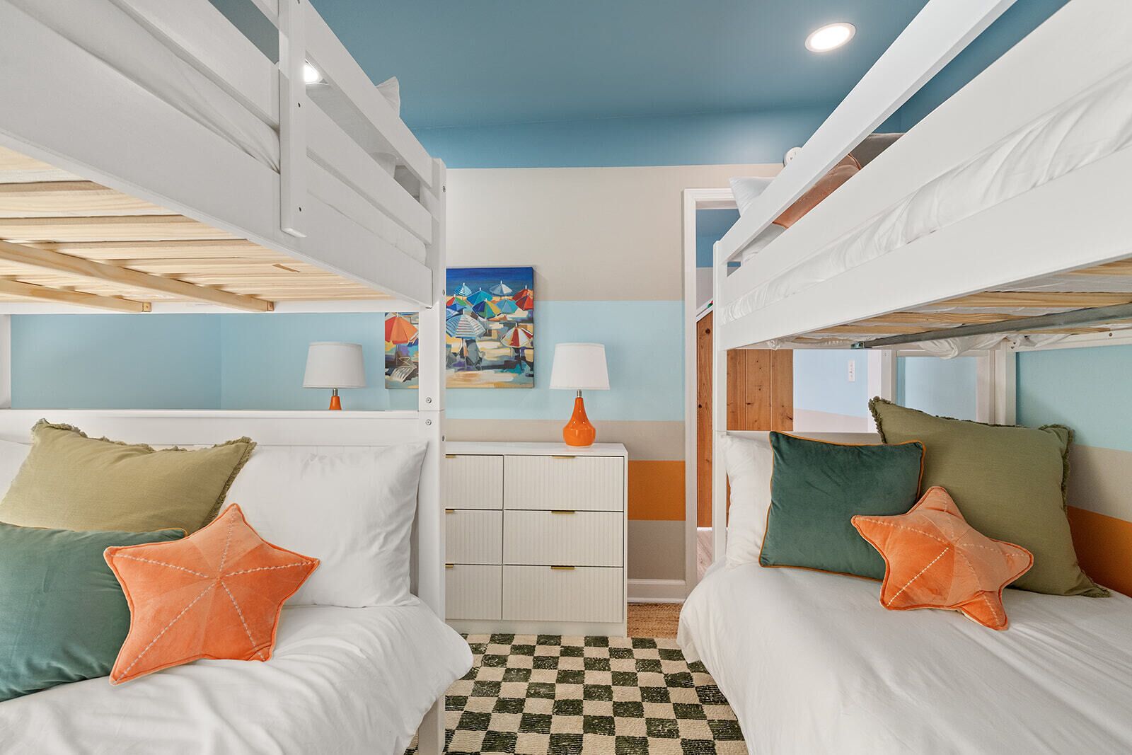 A room with bunk beds, a checkered floor, a painting, and a white dresser.