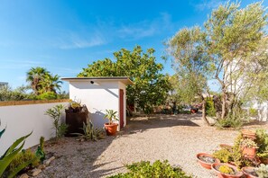 Un espace jardin agrémenté d’un bâtiment blanc, d’un chemin de gravier et de diverses plantes en pot.