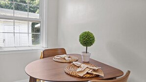 Mesa de jantar com dois individuais de palha, uma pequena planta em vaso e cadeiras de madeira.
