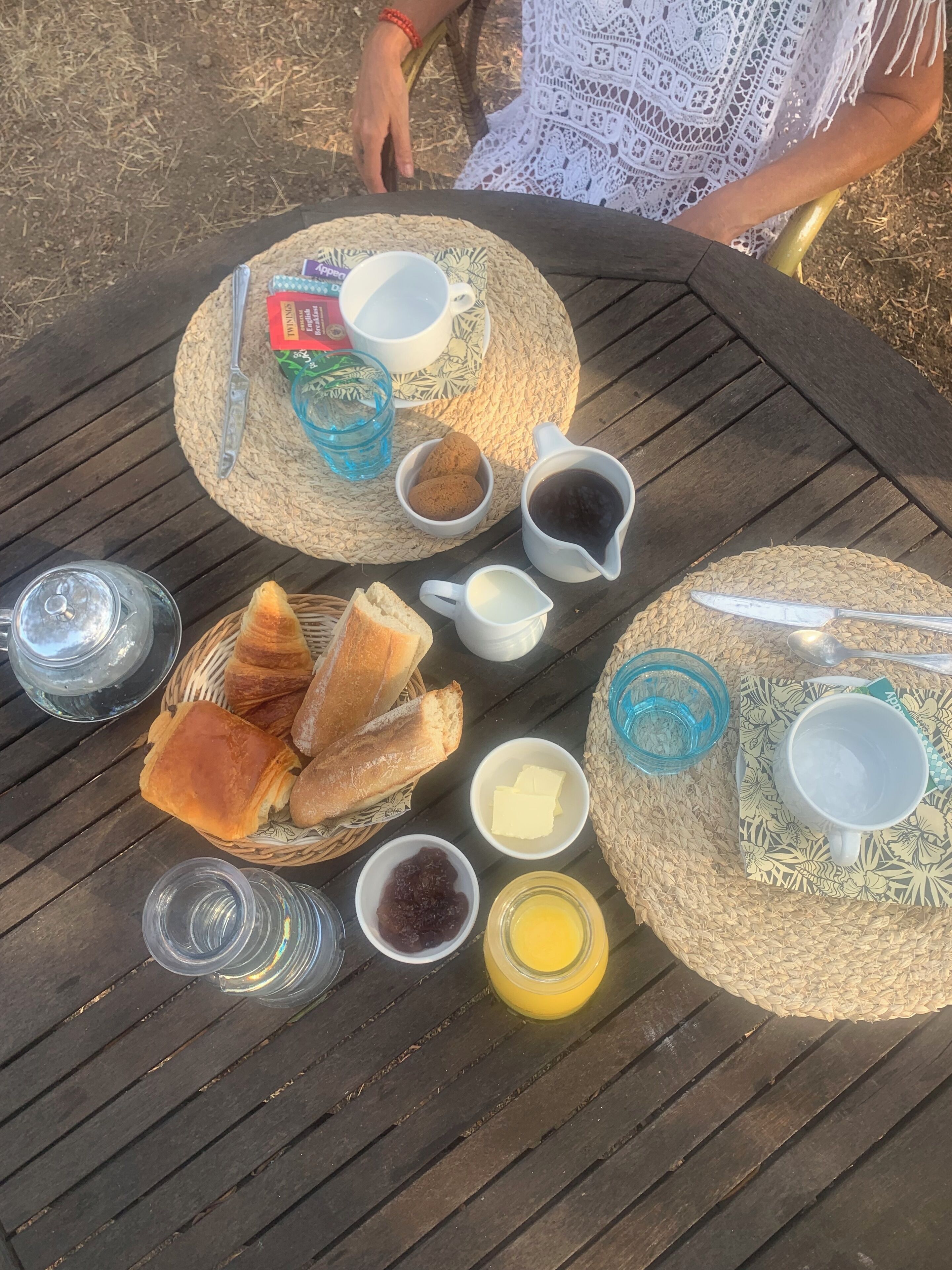 Une table dressée avec divers aliments et boissons, notamment du pain, du beurre, de la confiture et du café.