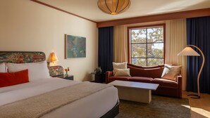 A hotel room with a large bed, a sofa, a coffee table, a floor lamp, and a window with curtains. - Hotel Daphne (Houston)