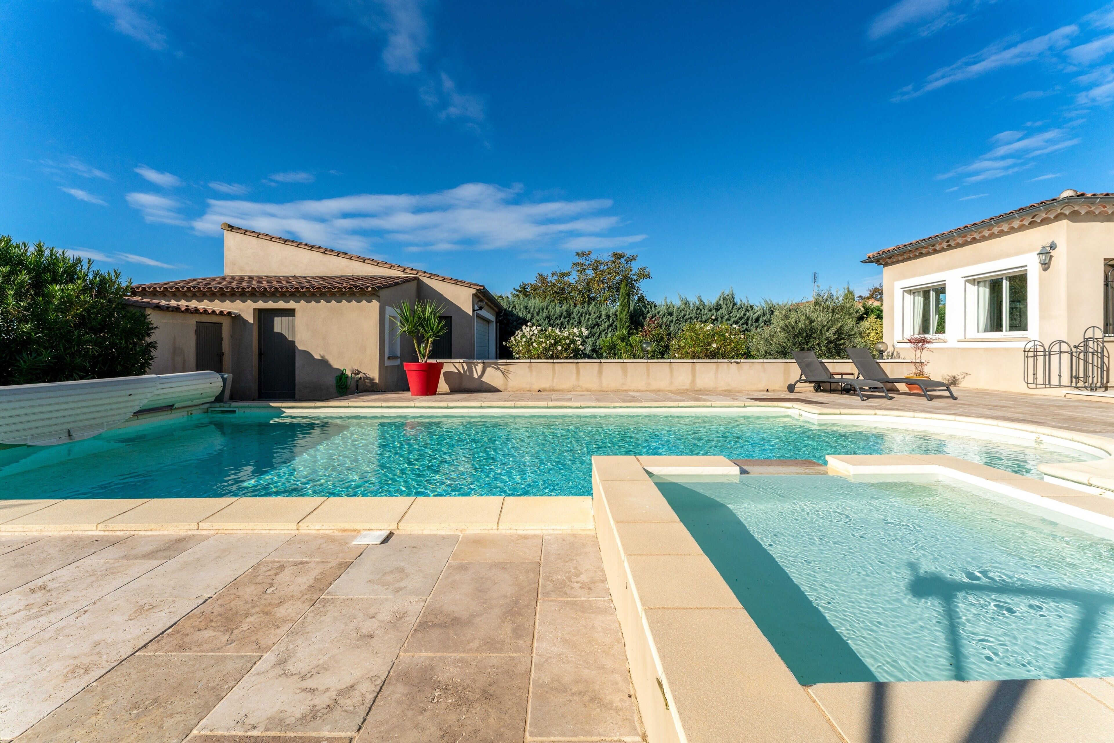 A swimming pool with a tiled deck, a small building with a door, and a potted plant.