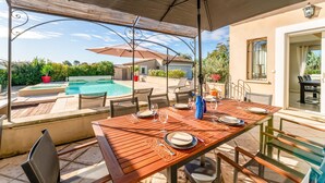 An outdoor dining area with a pool, chairs, and a table set for two.