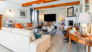 A living room with a sofa, coffee table, TV, fireplace, and wooden beams.