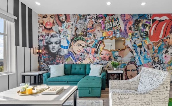 Una sala de estar con llamativa pared de grafitis, sofá color turquesa y una mesa de centro con bandeja.