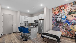 Ein kompaktes Apartment mit Küchenzeile, einem Bett und einem farbenfrohen Wandgemälde.
