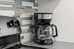 A coffee maker with a clear glass carafe and a black base, placed on a countertop with a tiled backsplash.