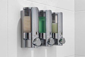 Dispensador montado en la pared con cuatro compartimentos etiquetados como acondicionador, champú, gel de baño y jabón.