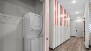 A laundry room with a washing machine and dryer, a hallway with lockers, and a door leading to another room.