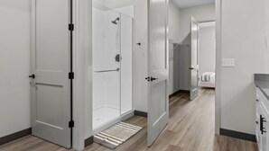 A modern bathroom with a glass shower enclosure, a visible towel rack, and a wooden floor.