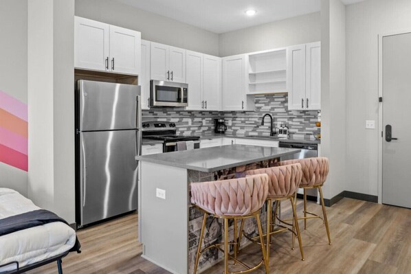 A modern kitchen with white cabinets, stainless steel appliances, a marble countertop, and a bar stool area.