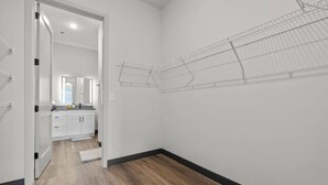 Un couloir étroit doté d’un plancher en bois, de murs blancs et d’une porte donnant sur un espace cuisine.