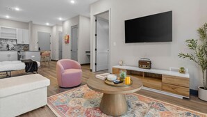 Un salon moderne avec un canapé, un fauteuil rose, une table basse et un téléviseur fixé au mur.